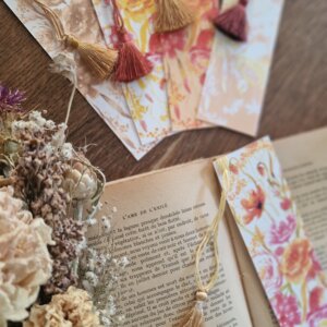 présentation de cinq marque-pages artisanaux, décorés de fleurs et d'un ruban avec gland décoratif. Fait main par Rosana Illustration